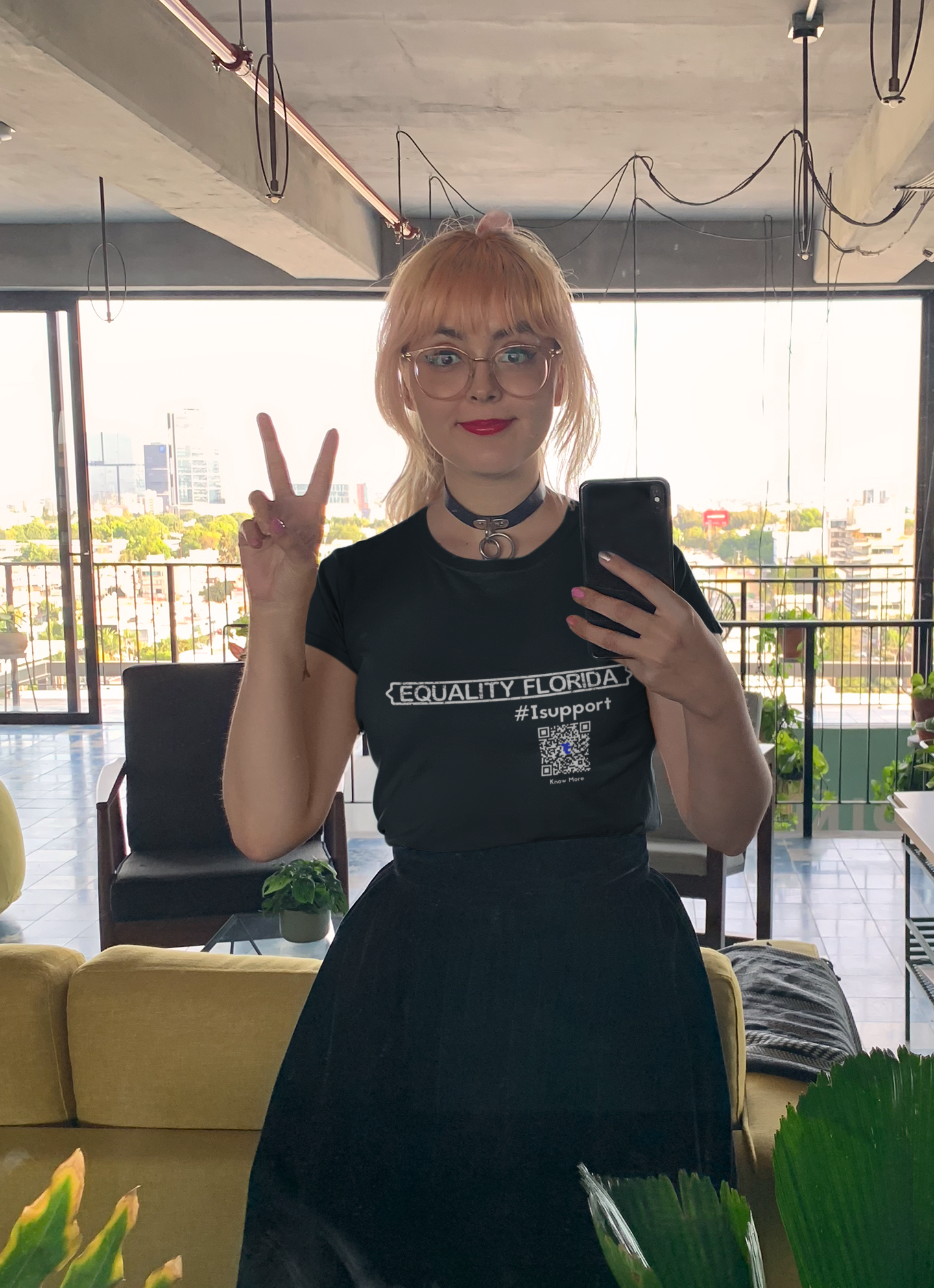 Blonde, female, presenting person taking a selfie and giving the peace sign in the mirror. She is wearing a full  long black skirt with her CLAIM It Tee™ that reads {EQUALITY FLORIDA} #IFightFor