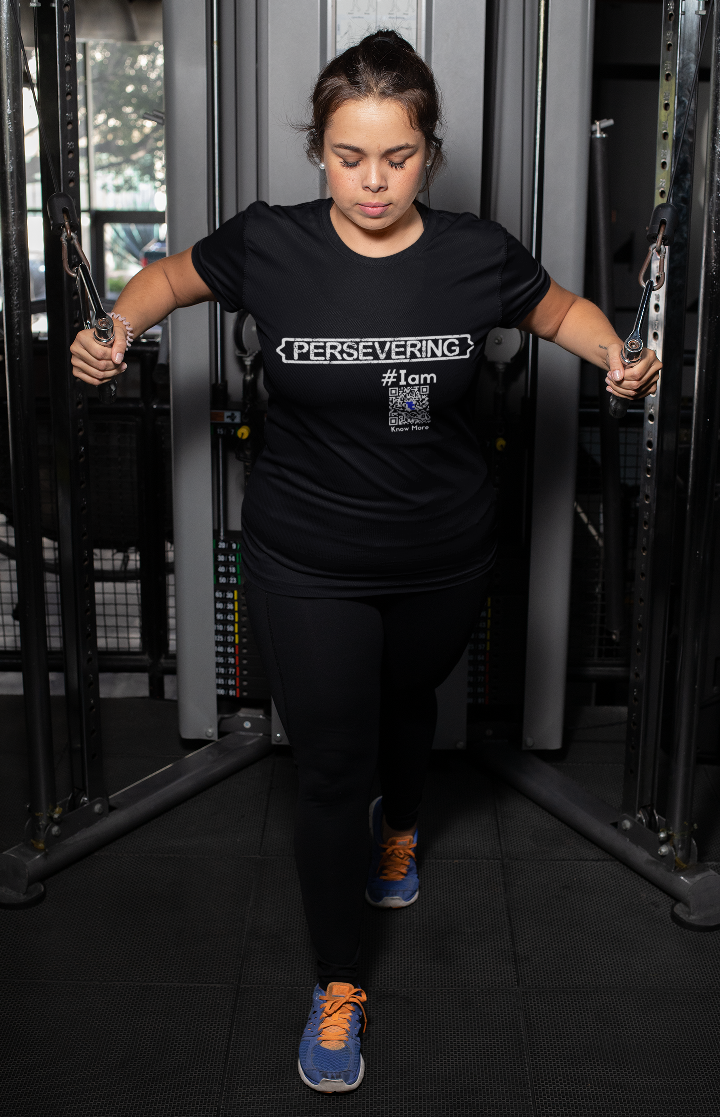 A female presenting person, using an arm weight training machine, is wearing a black CLAIM It Tee™. The CLAIM™ on the shirt reads {PERSEVERING} #Iam.
